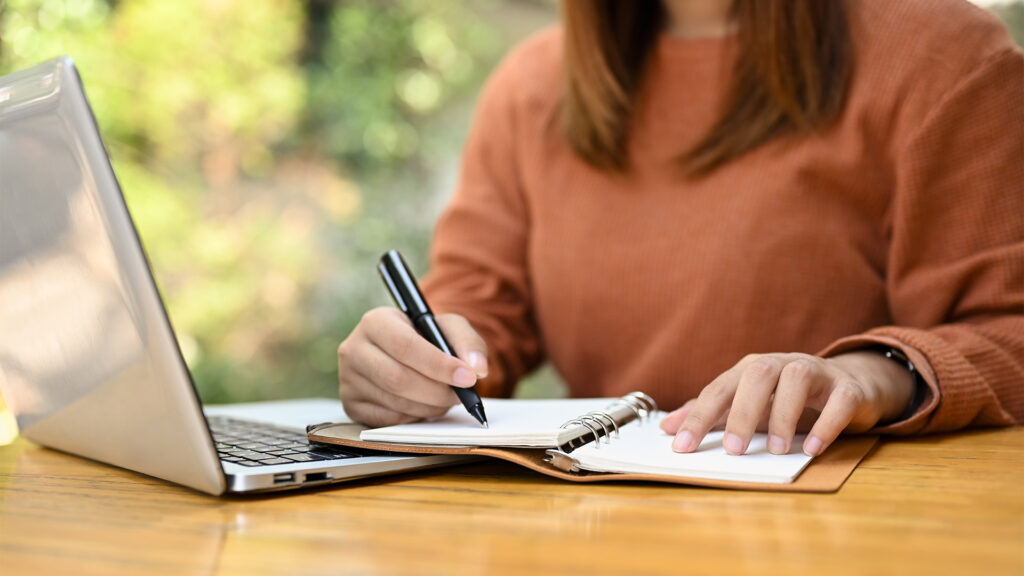 Female freelancer using laptop and writing notes in personal daily planner